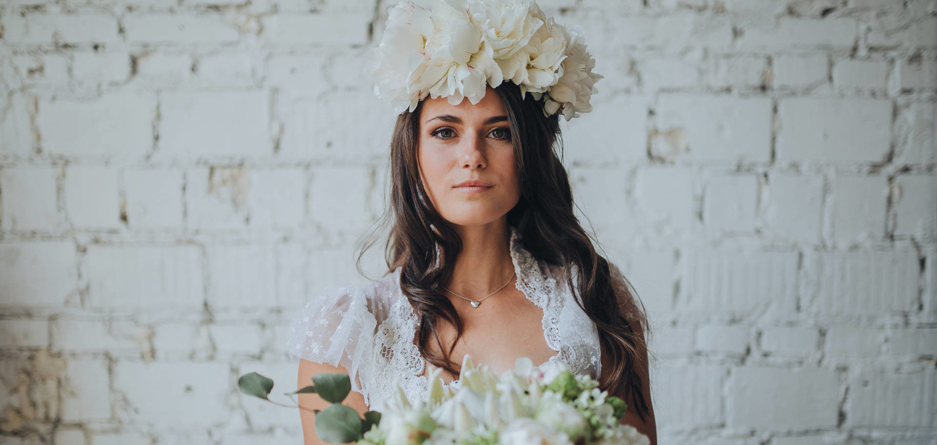 Braut mit Blumenstrauss vor weisser Wand